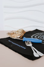 Load image into Gallery viewer, Oyster shucking tool with blue handle on a black towel with 'Mothershucker' branding.