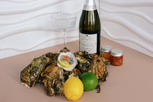Load image into Gallery viewer, Mersea Oysters on a plate with a bottle of Prosecco and condiments on a beige surface.