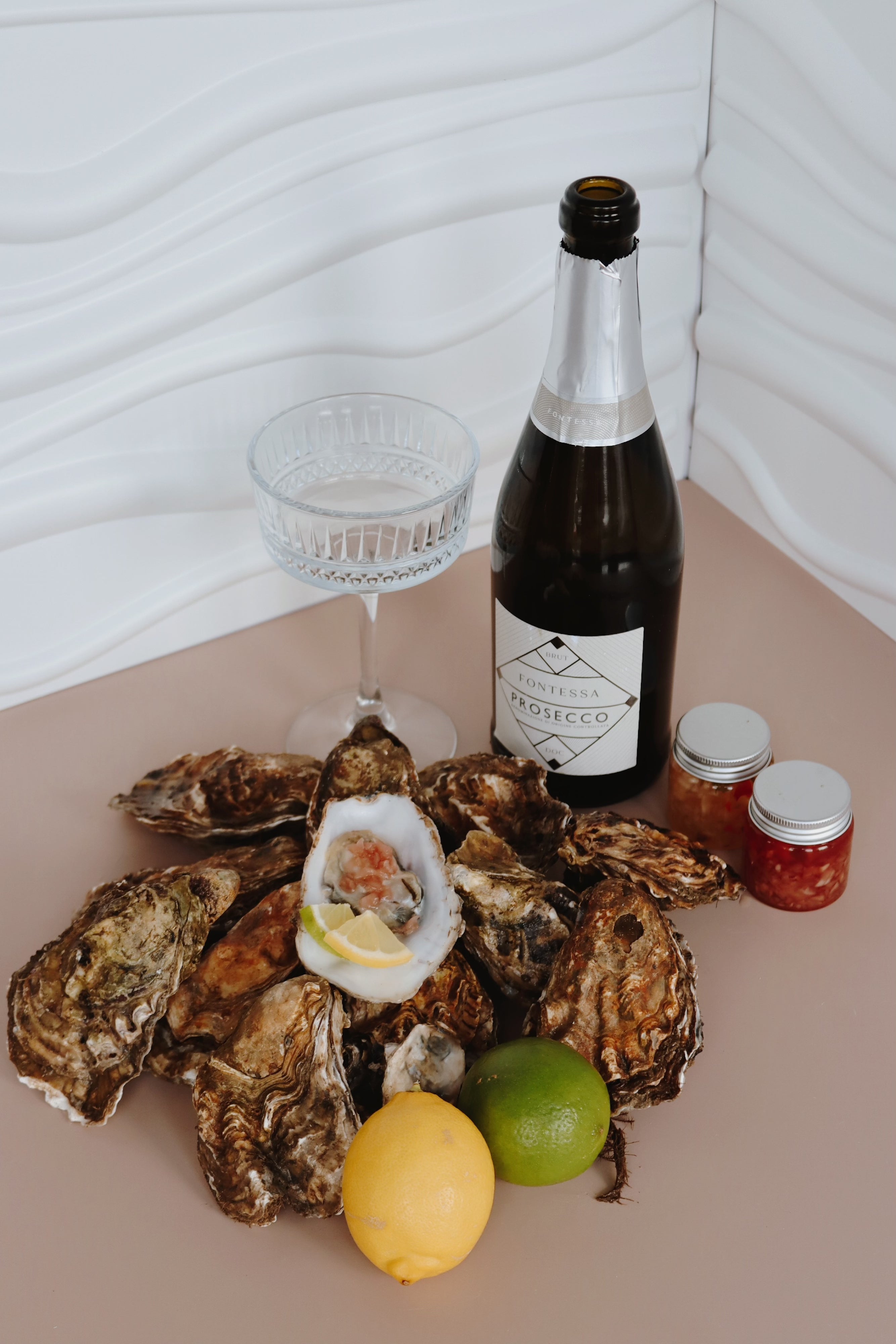 Mersea Island rock Oysters on a half shell with a bottle of wine, glass, and condiments on a white surface.