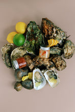 Load image into Gallery viewer, Mersea Oysters on the half shell with lemon wedges and a small container of sauce on a beige background
