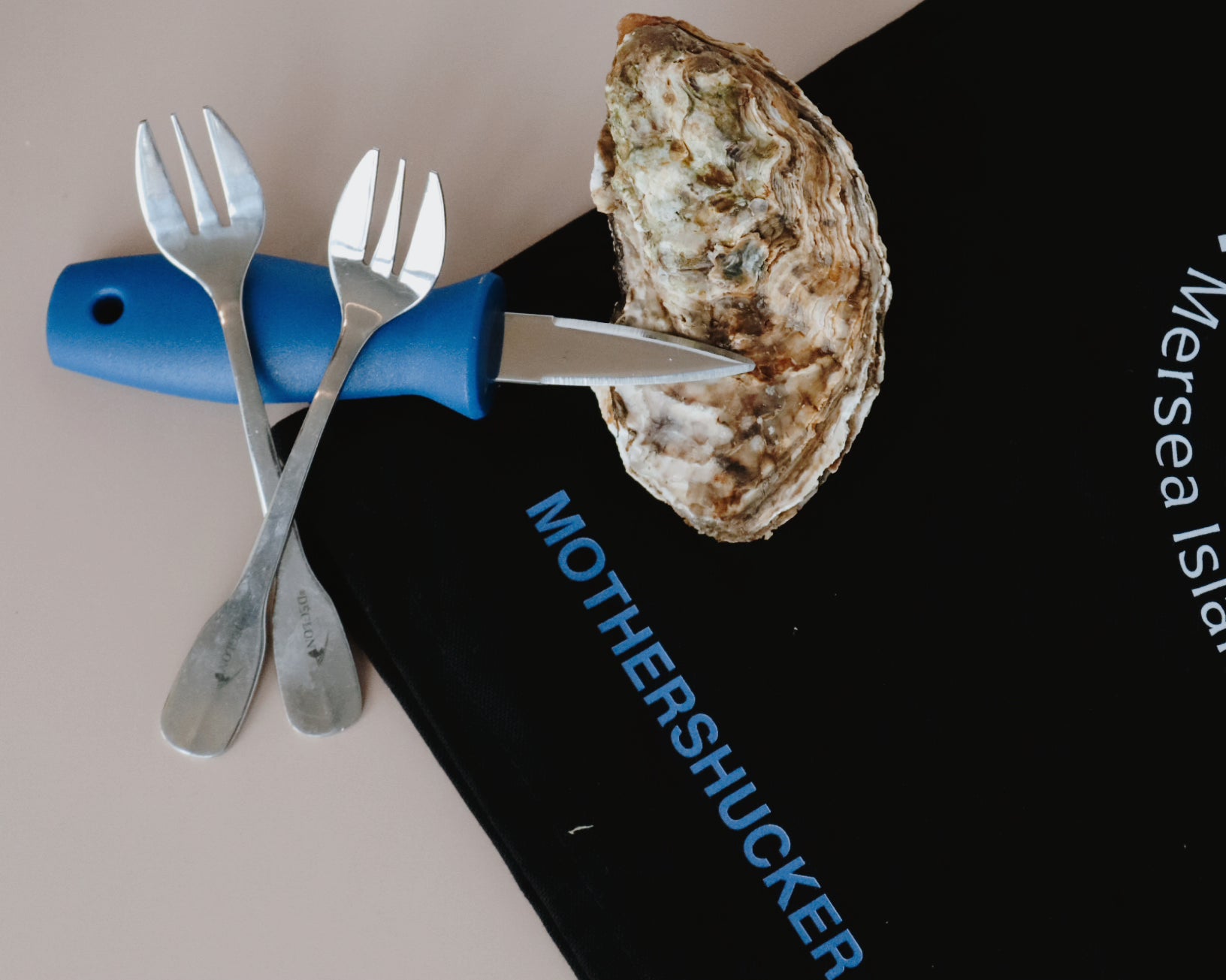 Oyster shucking tool with two forks and an oyster on a black surface.