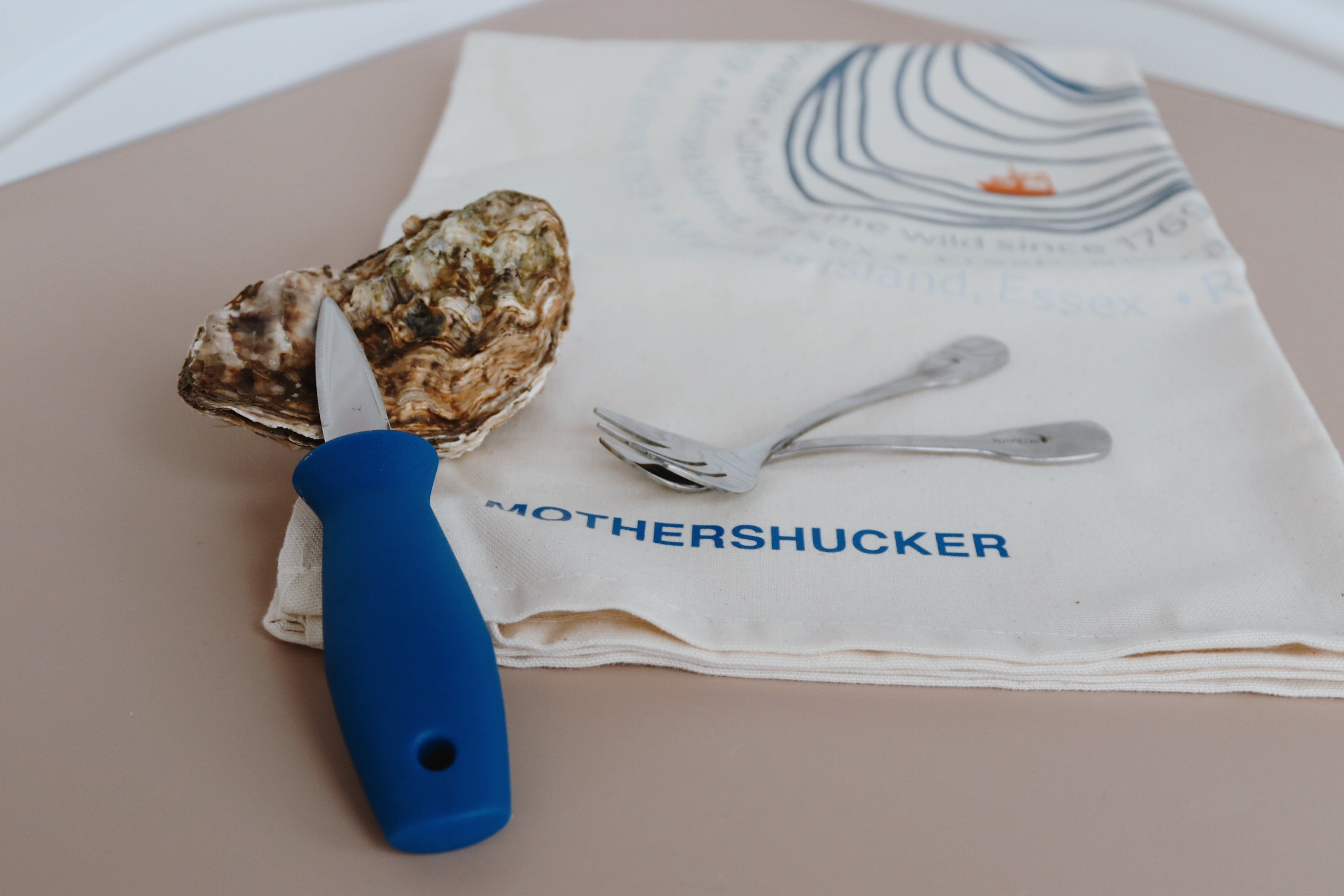 Oyster with a knife on a towel with 'Mothershucker' text. Shucking bundle 